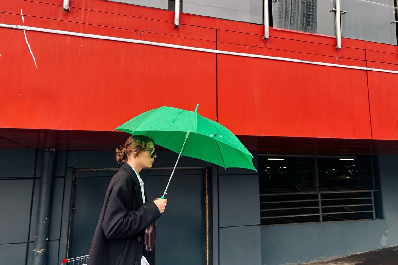 Thoughtful woman with a green umbrella walks past a bright red building, symbolizing inner emotions, suppressed anger, and reconnecting with one’s feelings