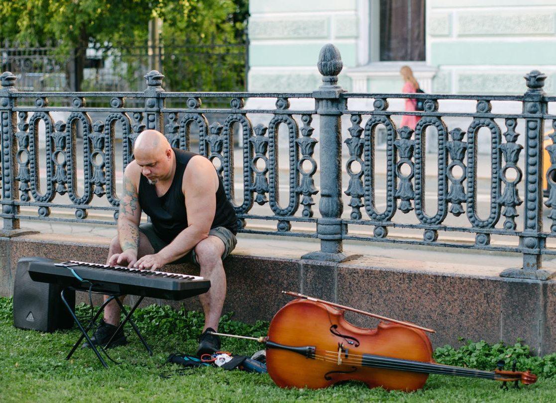 Balding man playing a keyboard outdoors next to a cello, symbolizing the impact of age and lifestyle on hair loss